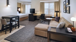 Una habitación de hotel con una cama, un escritorio con una computadora, un sofá, una mesa de centro y un teléfono.