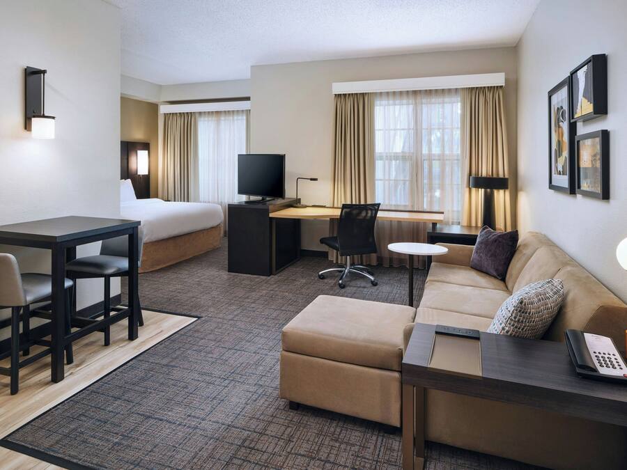 A hotel room with a bed, a desk with a computer, a sofa, a coffee table, and a telephone.