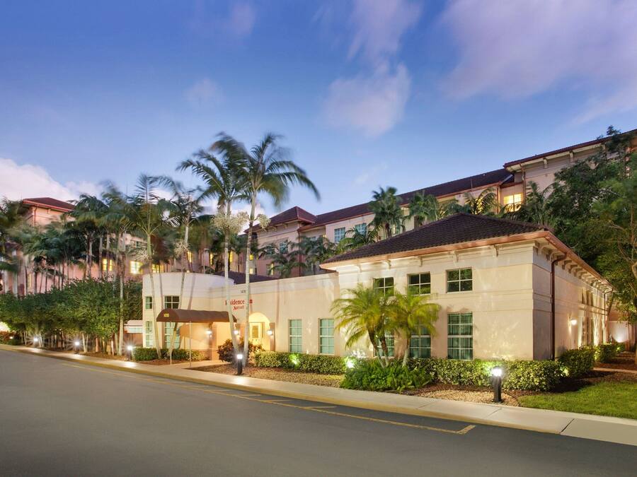 A hotel with a modern architectural style, featuring a well-maintained lawn, palm trees, and a clear sky.