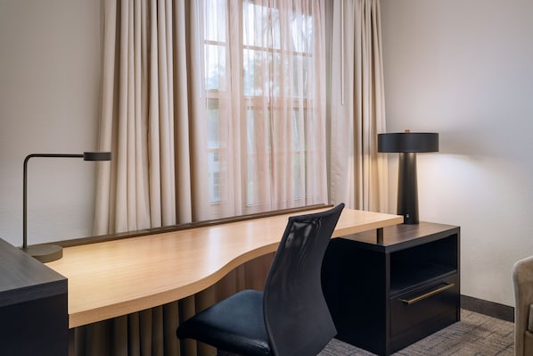 A modern hotel room with a curved desk, a black mesh chair, a lamp, and a view through sheer curtains. - Residence Inn by Marriott Fort Lauderdale SW Miramar (Miramar)