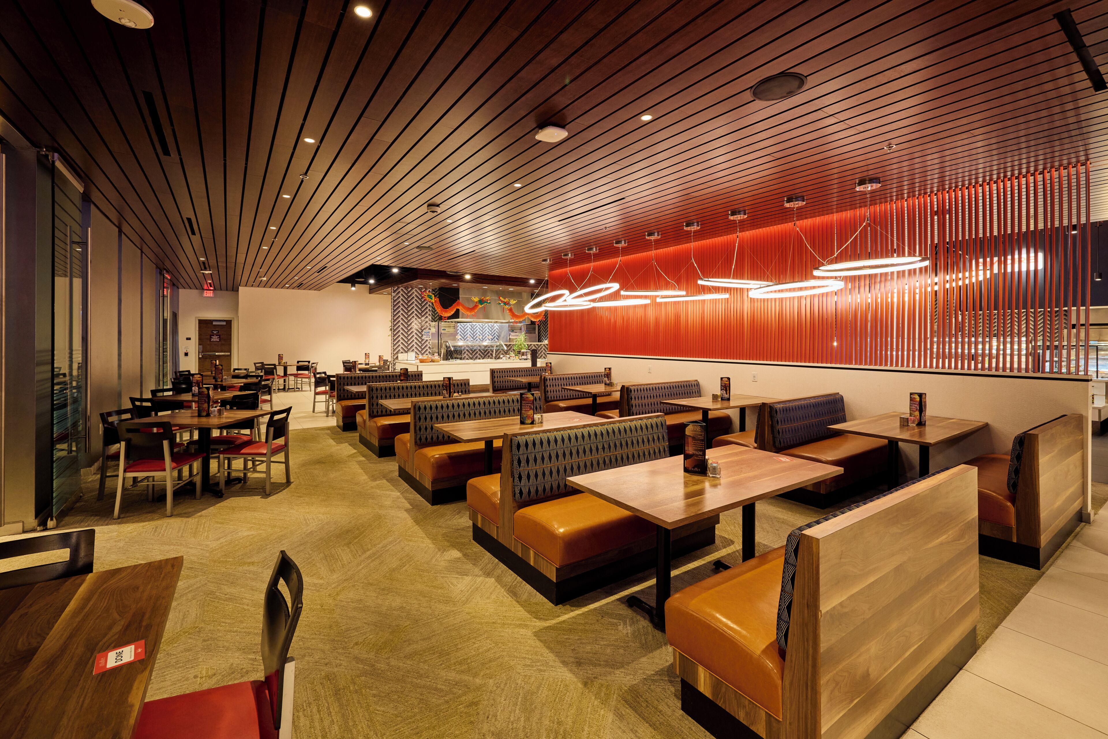 Un intérieur de restaurant moderne avec des banquettes, des tables en bois et un mur d’accent rouge.
