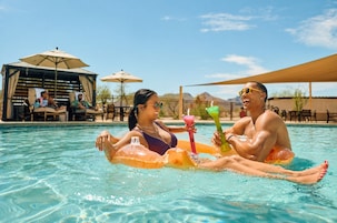 Uma piscina com pessoas em boias, cadeiras de descanso e guarda-sóis ao fundo.