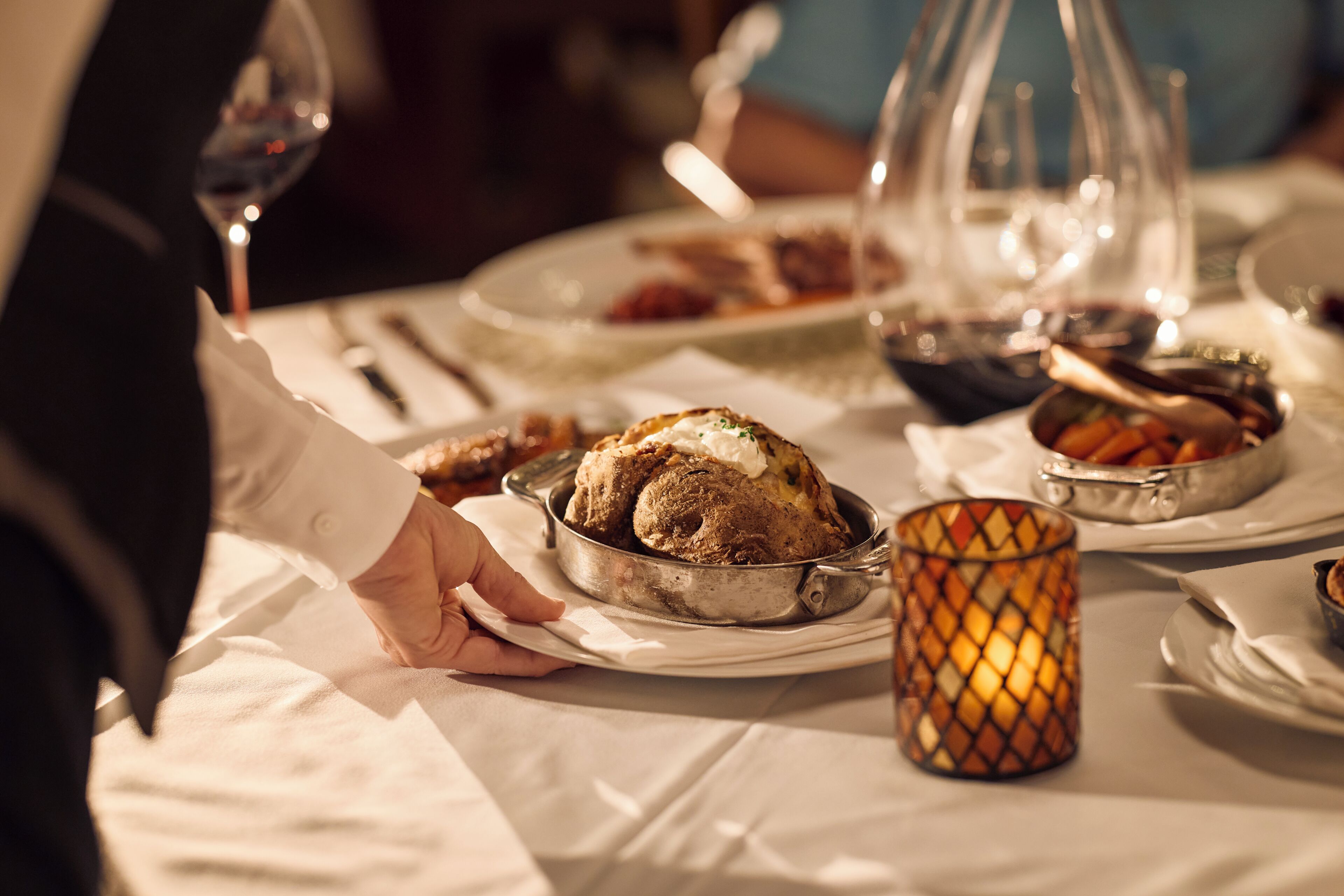 Una mesa de comedor con un pavo asado como plato principal, un candelabro de vidrio y diferentes fuentes de comida.