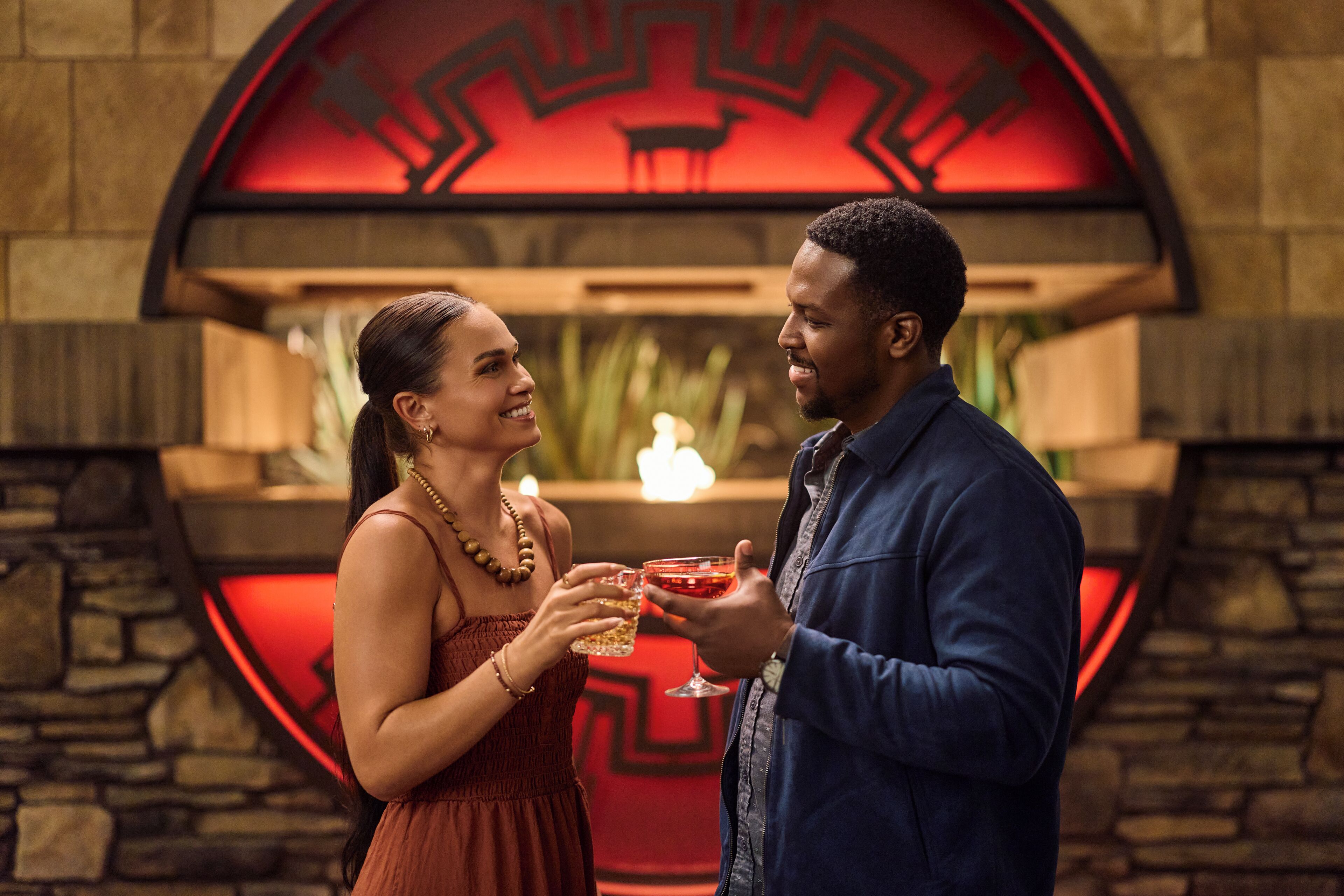 A couple holding drinks in a room with a circular red design on the wall.