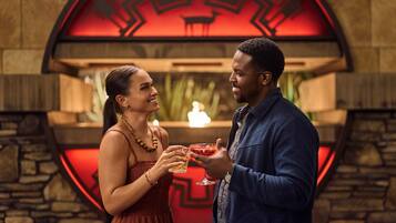 A couple holding drinks in a room with a circular red design on the wall.