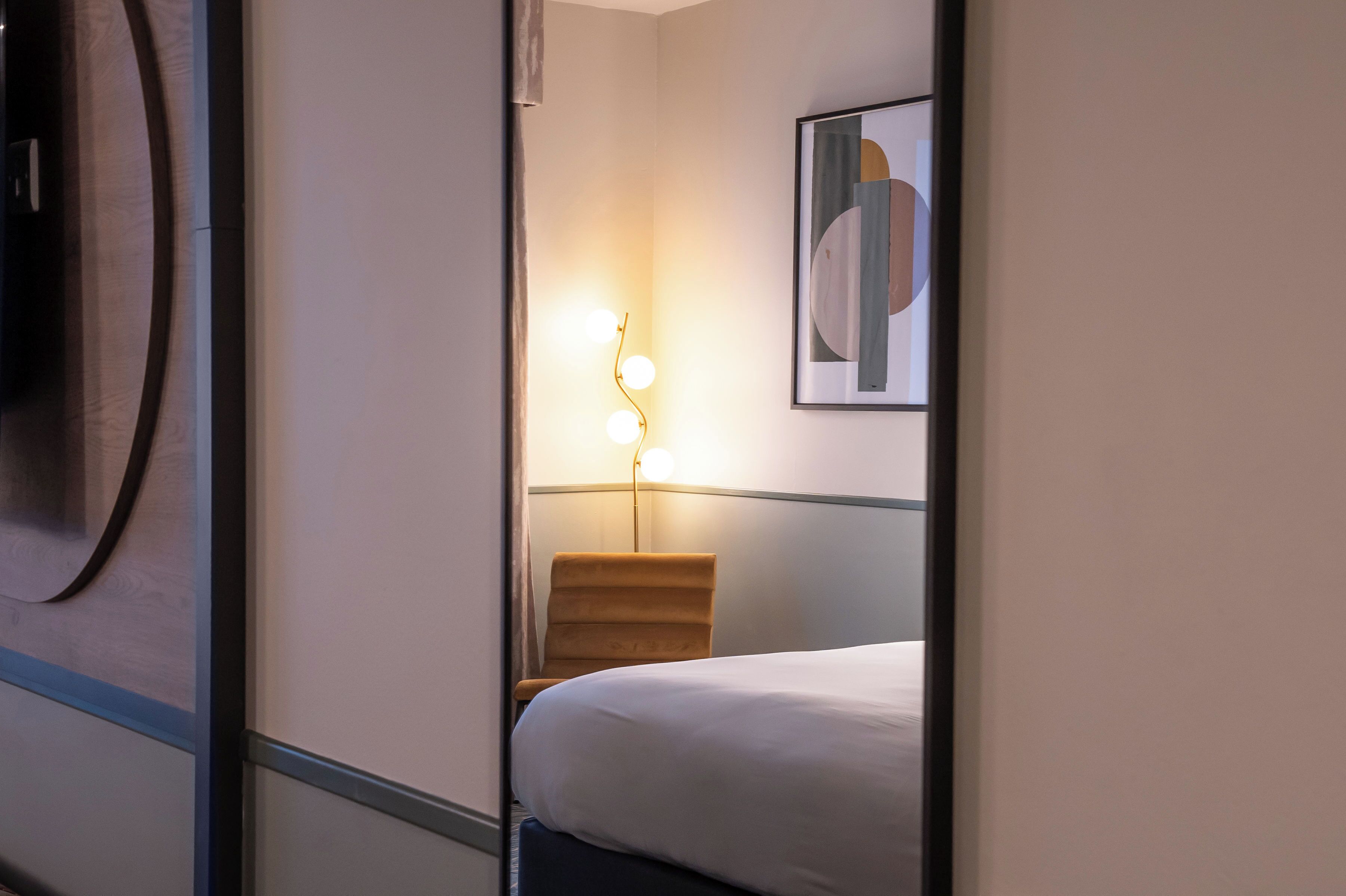 A hotel room with a bed, a wall-mounted artwork, and a floor lamp.