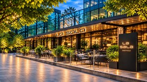 An outdoor dining area with tables and chairs, a modern building facade, and a sign that reads 'LA SALA SHEFFIELD'.