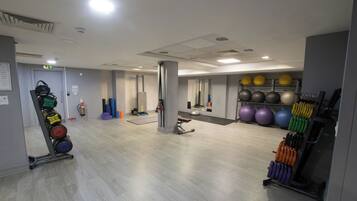 Un gimnasio con equipo de ejercicio, un espejo y un estante para pelotas en la pared.