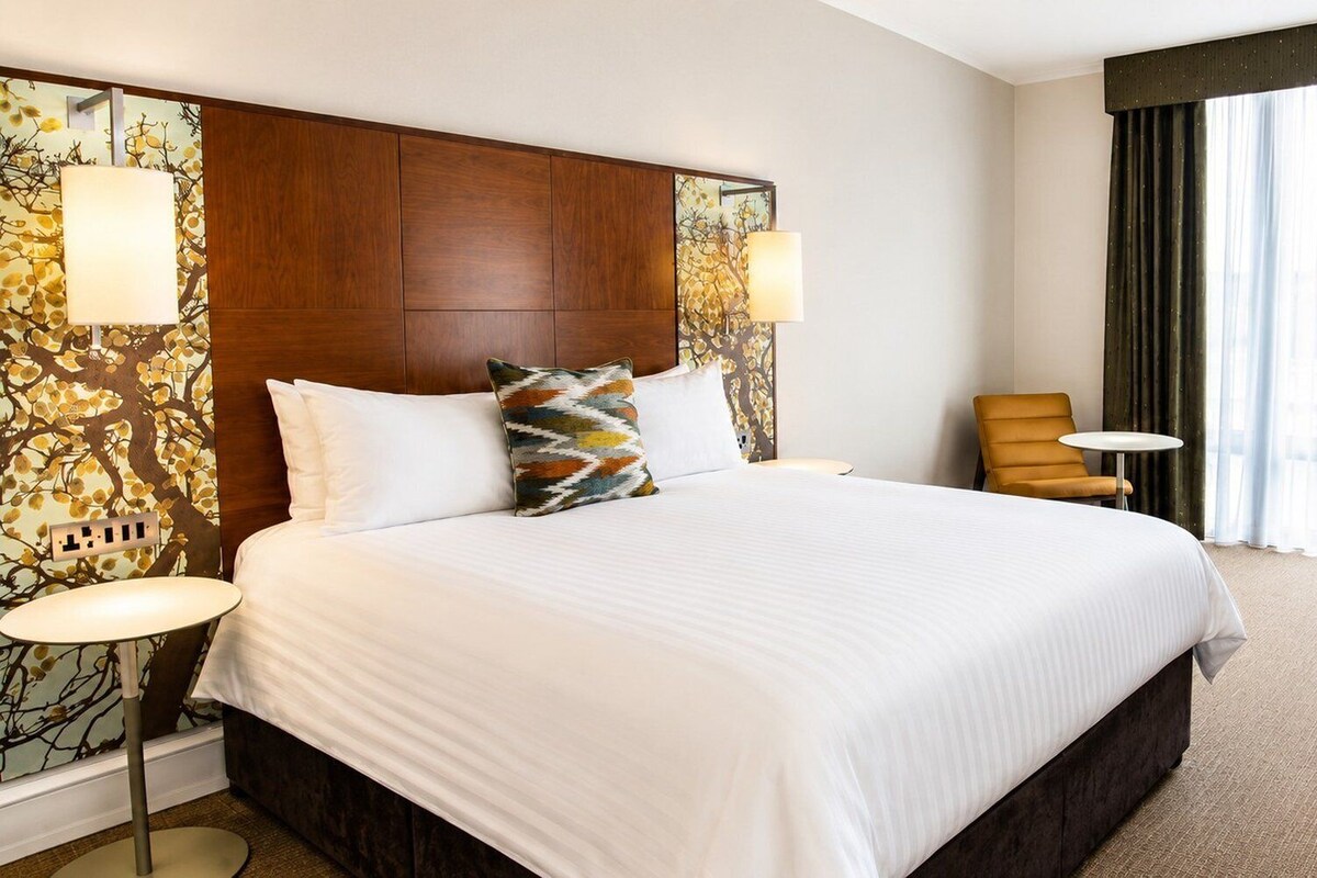A hotel room with a large bed, a desk, a chair, and a view of the outdoors.