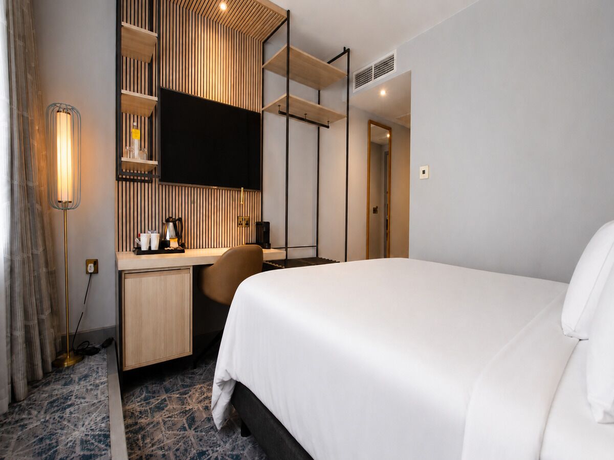 Una habitación de hotel con cama, escritorio, televisor y espejo.