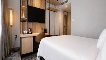 Una habitación de hotel con cama, escritorio, televisor y espejo.
