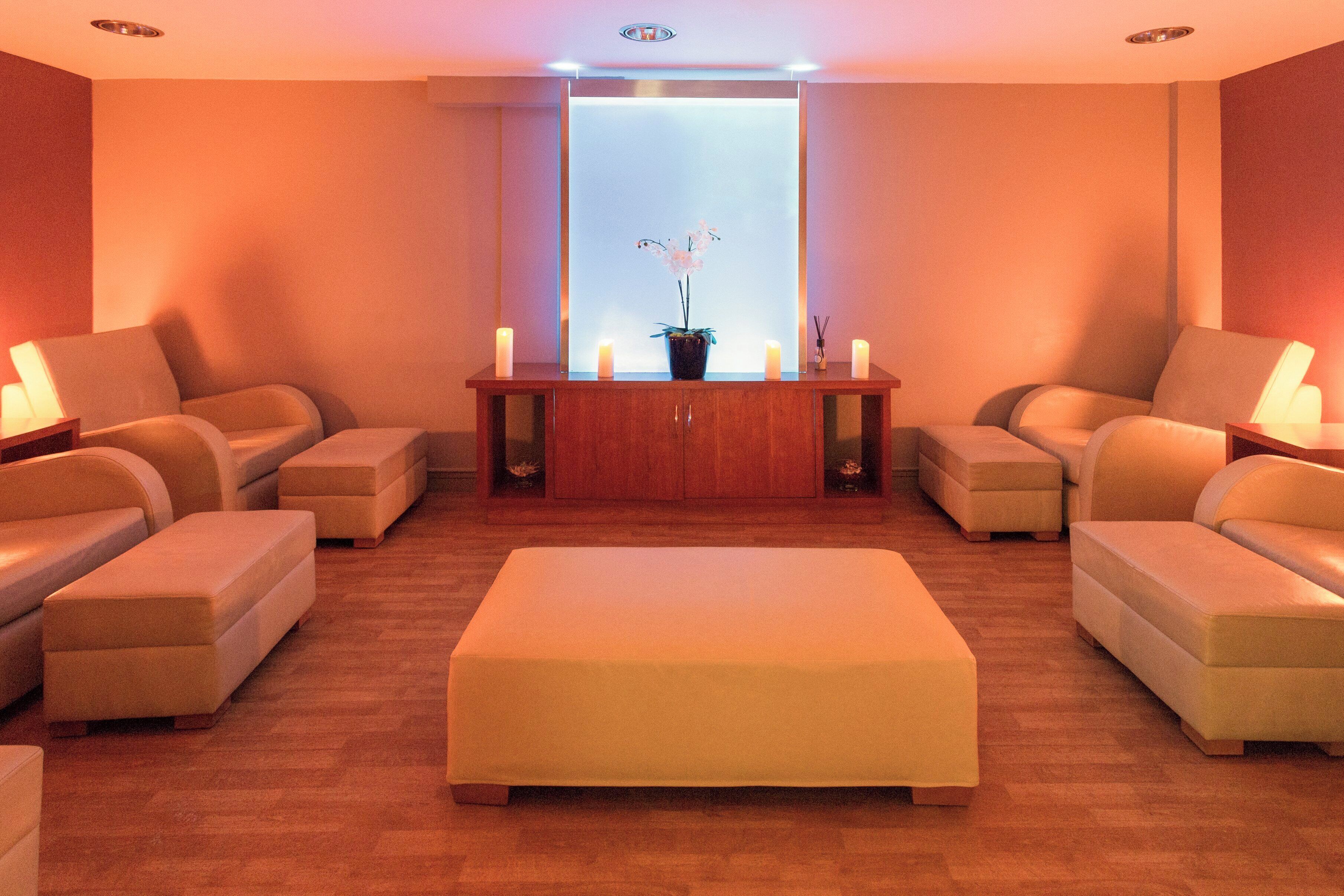 Un salón de spa con una mesa de madera en el centro, diversas opciones de asientos y un gran ventanal.