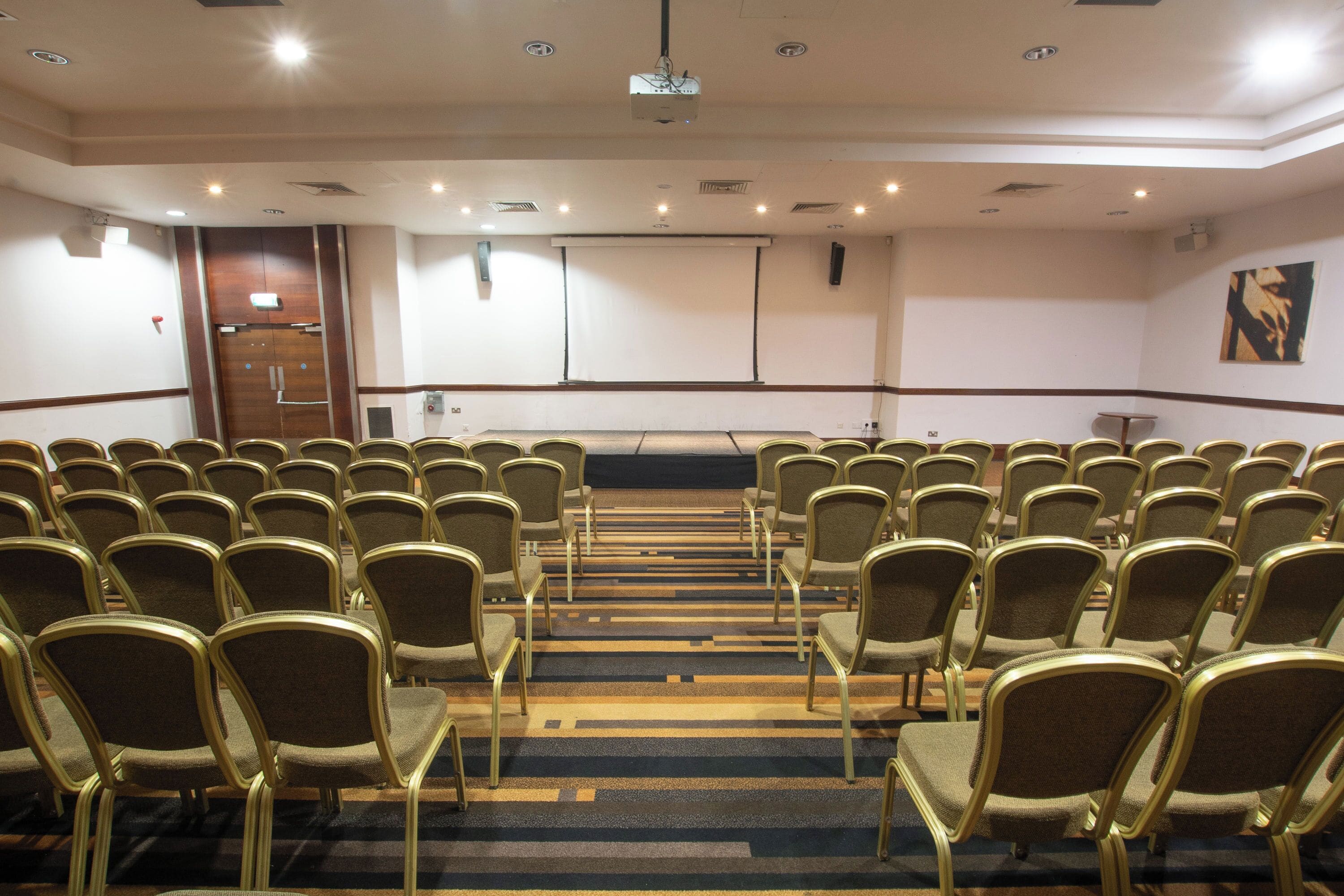 Ein Konferenzraum mit Reihen von Stühlen, einer Projektionsleinwand und einem Teppichboden.