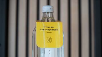 A clear glass bottle with a yellow label and a white cap, set against a blurred background.