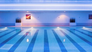 Una piscina con marcas de carriles, dos plantas en macetas y un cuadro en la pared.