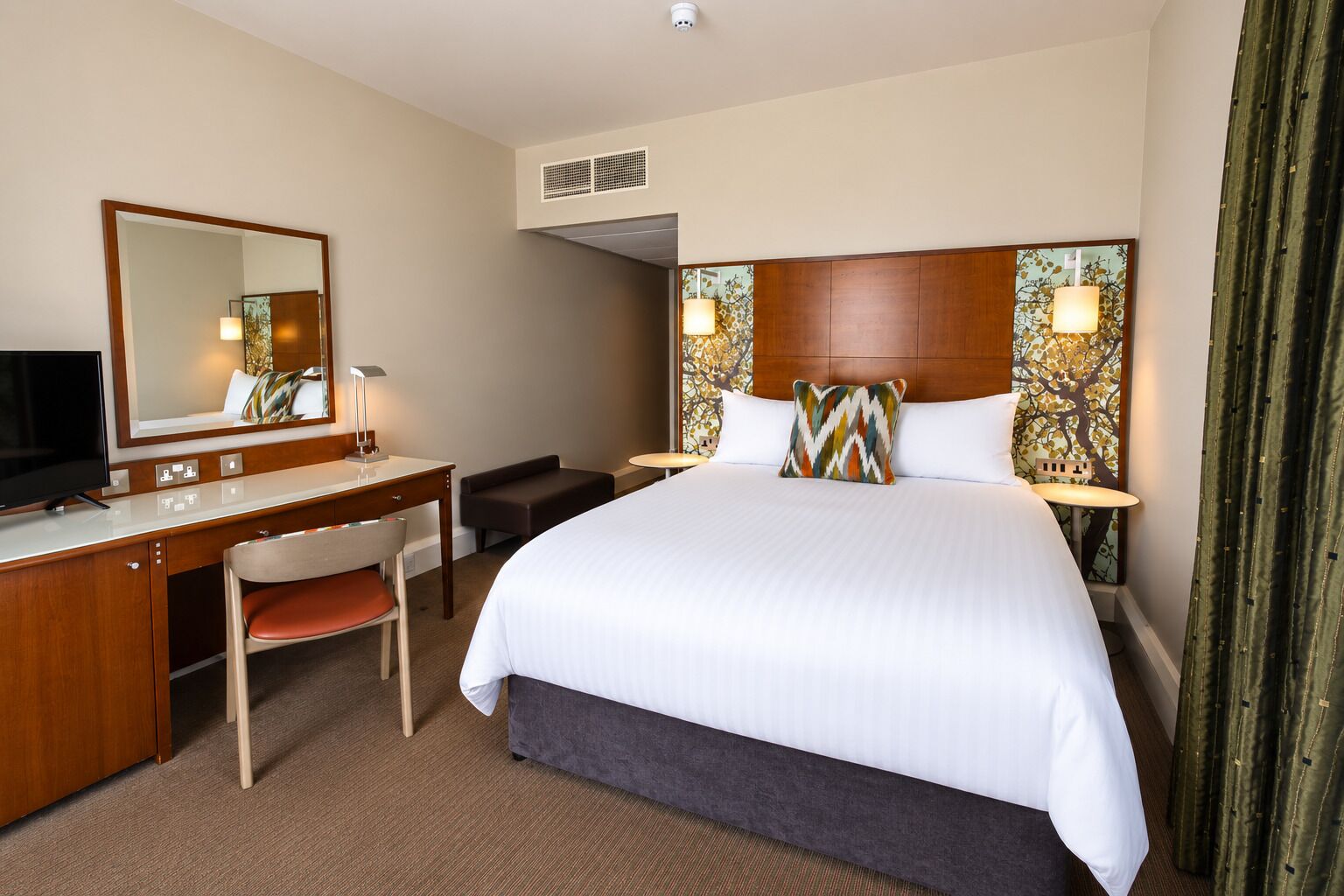 A hotel room with a bed, a desk, a chair, a television, and a large window.