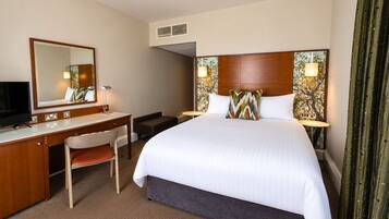 A hotel room with a bed, a desk, a chair, a television, and a large window.