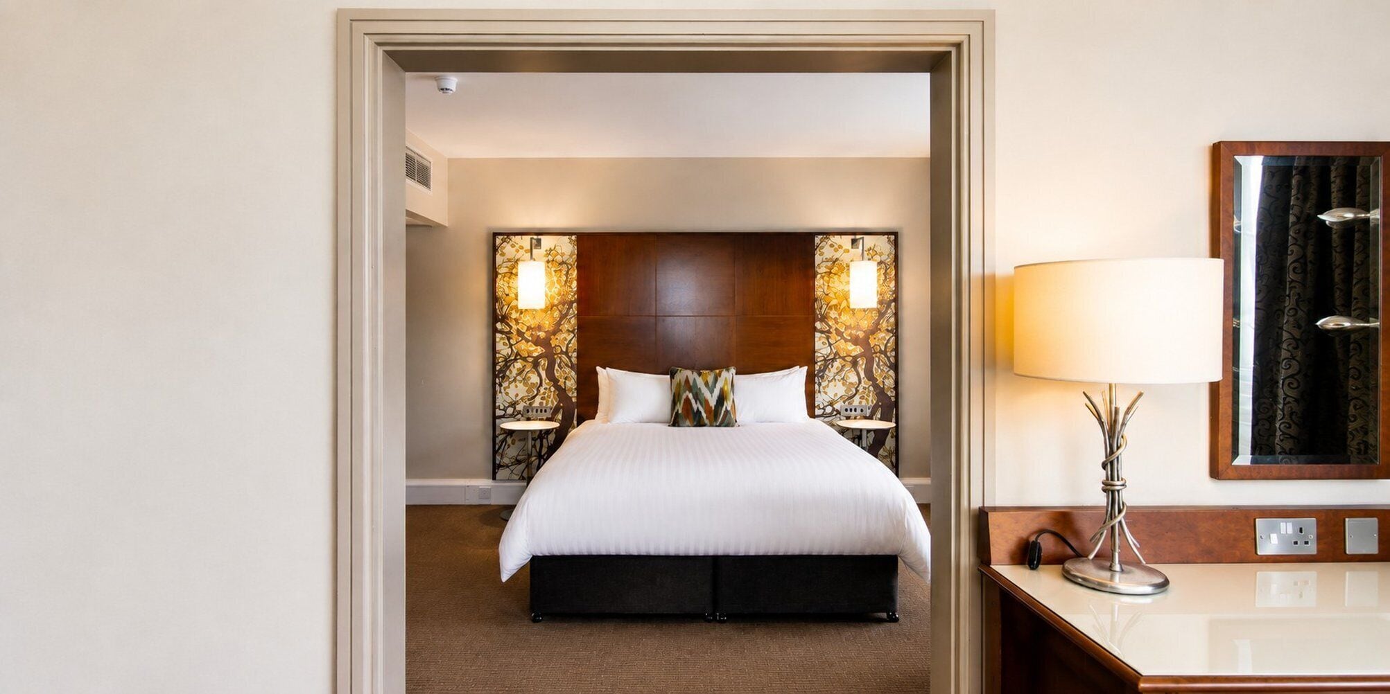Una habitación de hotel con cama, mesitas de noche, lámpara y espejo.