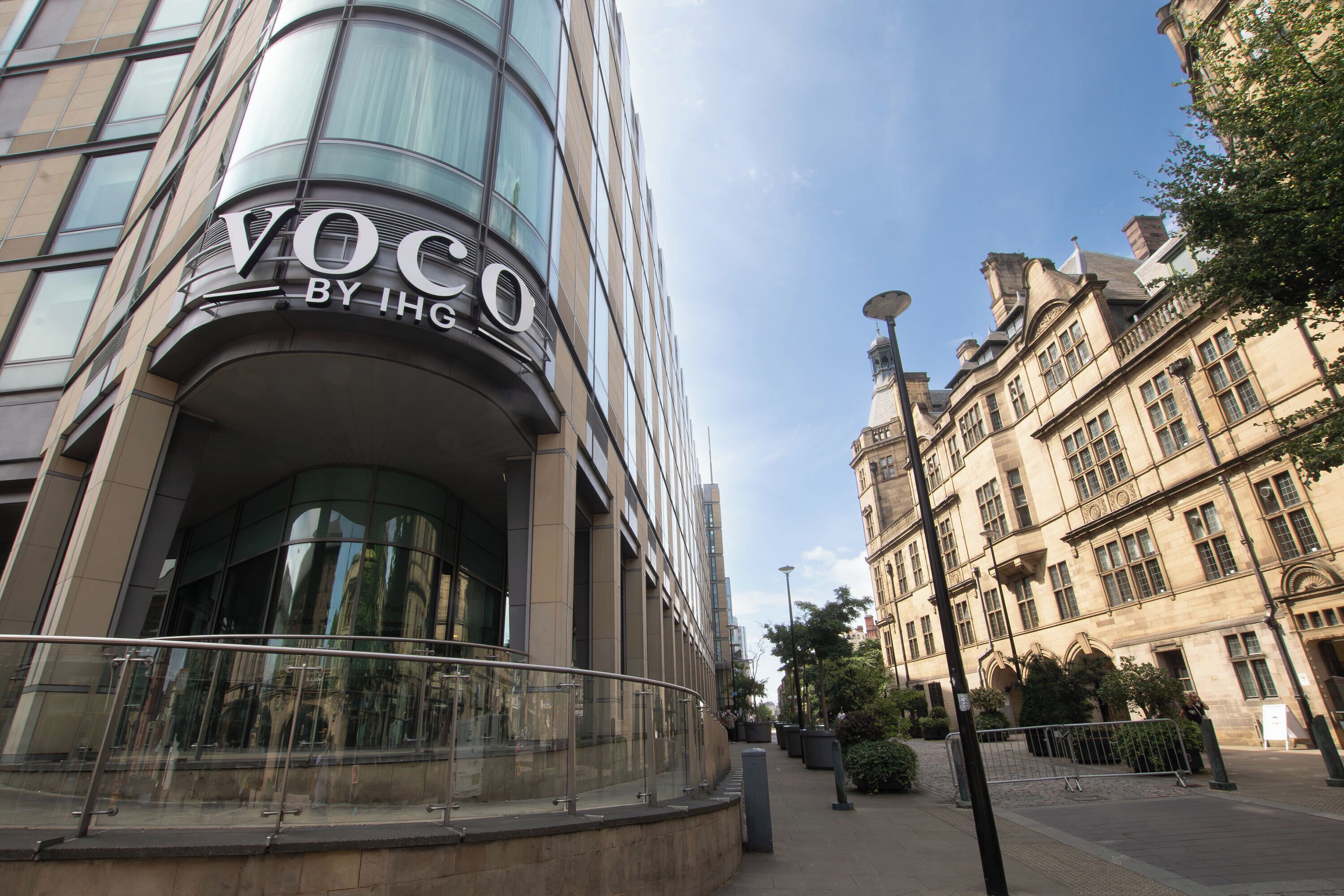 En modern byggnad med en böjd fasad och en skylt med texten ”Voco By IHG”.