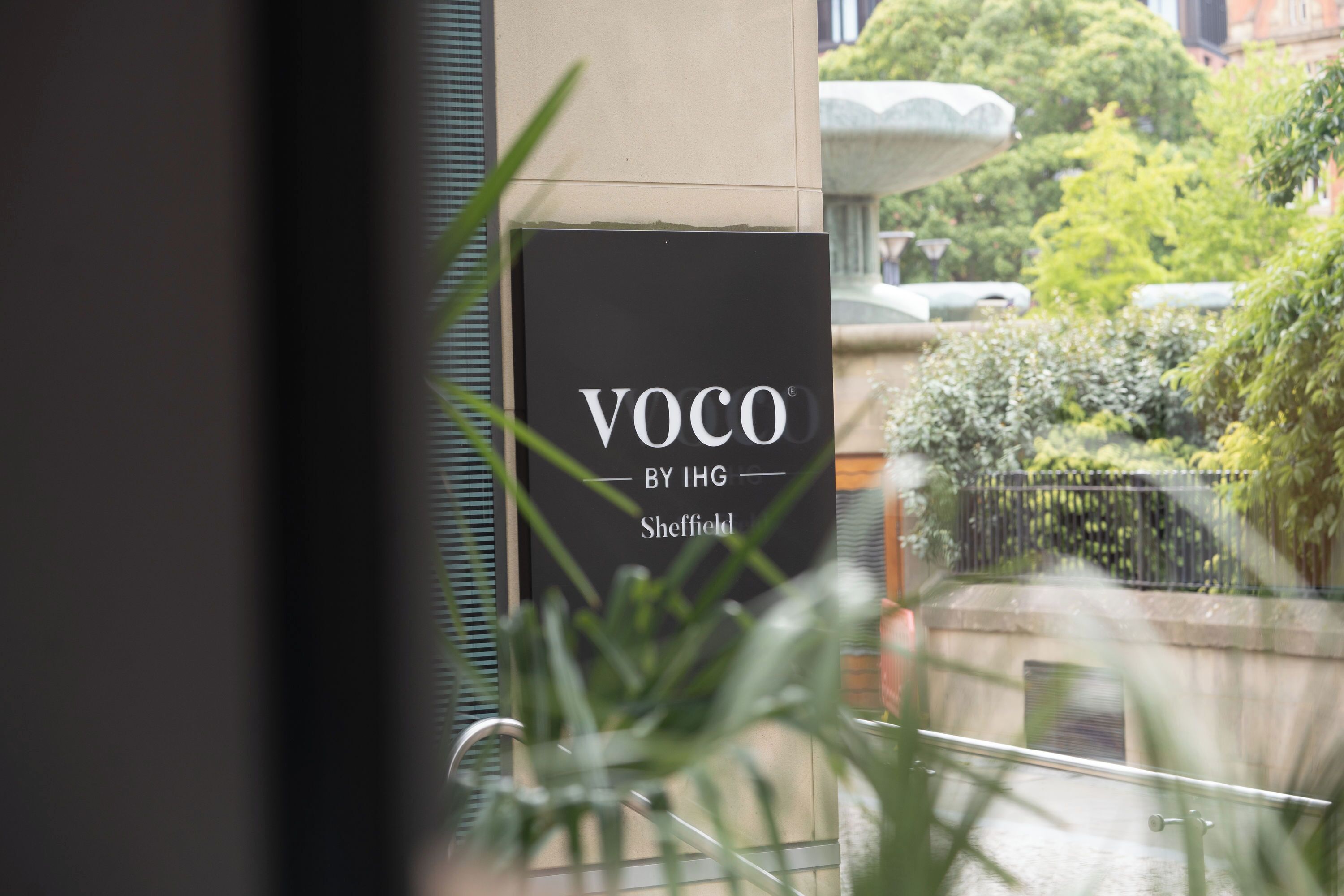 Letrero que dice 'VOCO BY IHG Sheffield', con vistas a un jardín y una fuente al fondo.