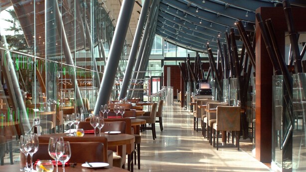 Un restaurante moderno con paredes de vidrio, mesas y sillas de madera.