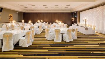 A banquet hall with tables set for a formal event, featuring white tablecloths and chairs with white sashes.