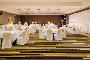 Un salón de banquetes con mesas dispuestas para un evento formal, con manteles blancos y sillas adornadas con cintas blancas.