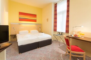Habitación de hotel con cama, escritorio con silla, televisor y un cuadro en la pared.