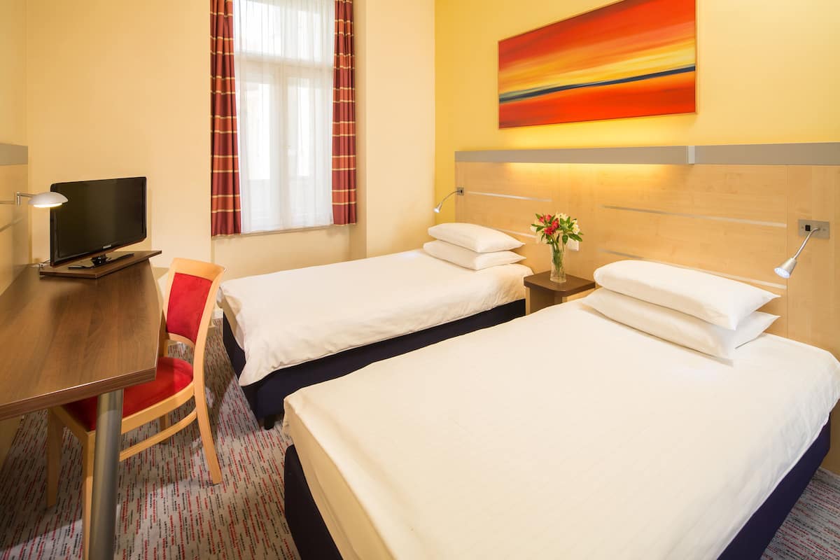 A hotel room with two beds, a desk, a TV, and a window with curtains.