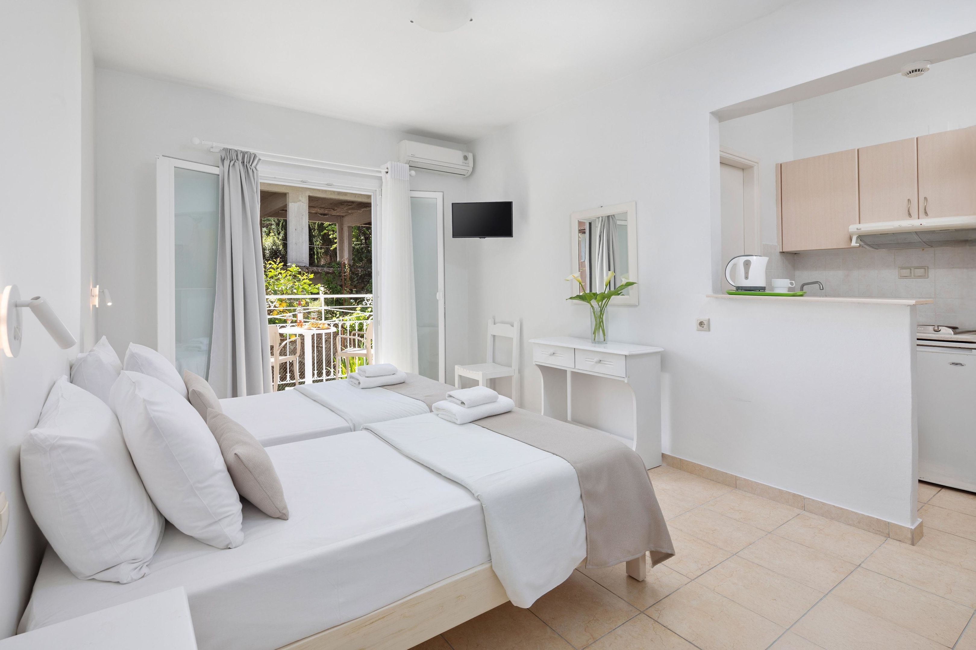 A hotel room with a bed, a desk, a TV, and a balcony with a view of greenery.