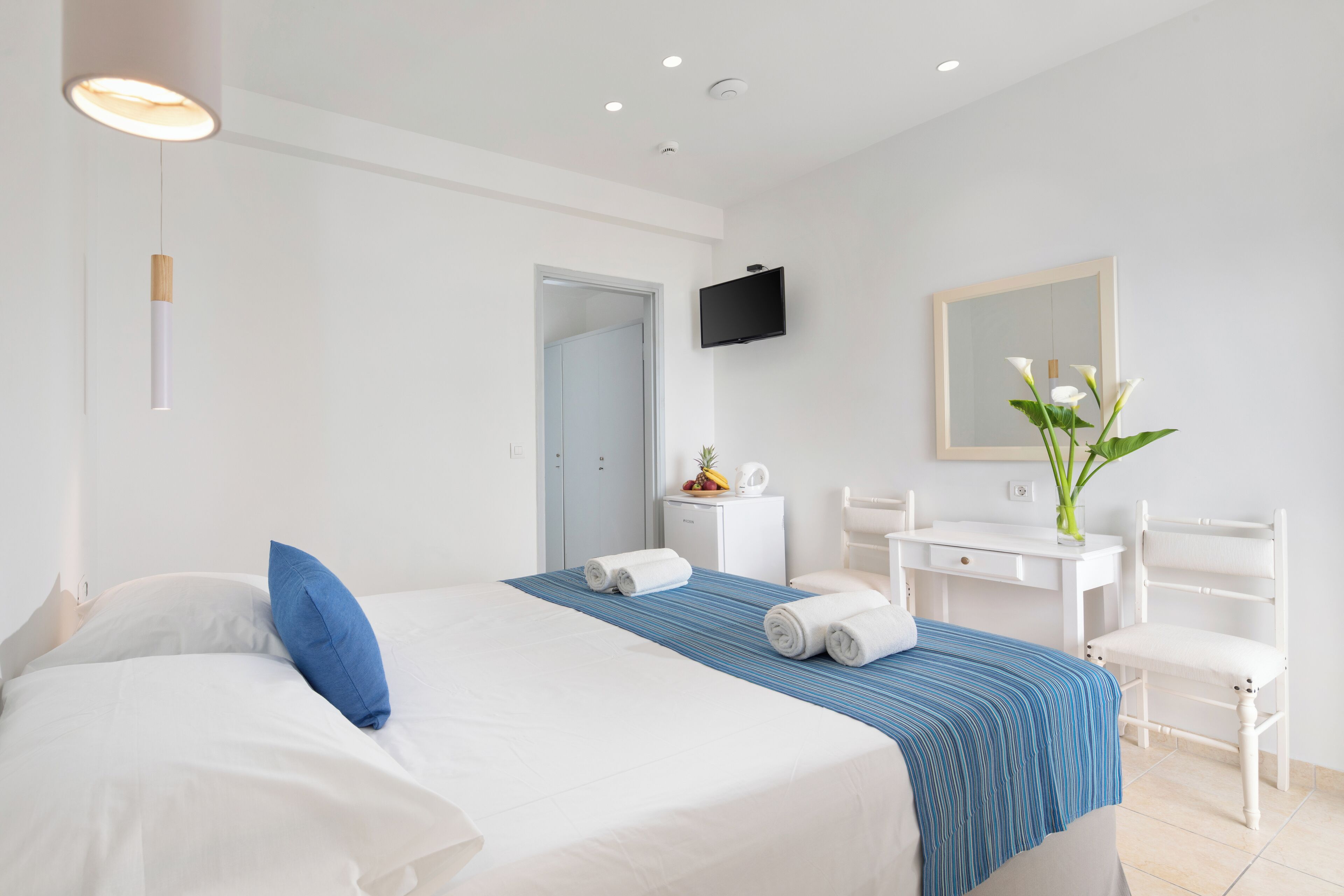 Una habitación de hotel con cama, escritorio, silla, televisor y espejo.