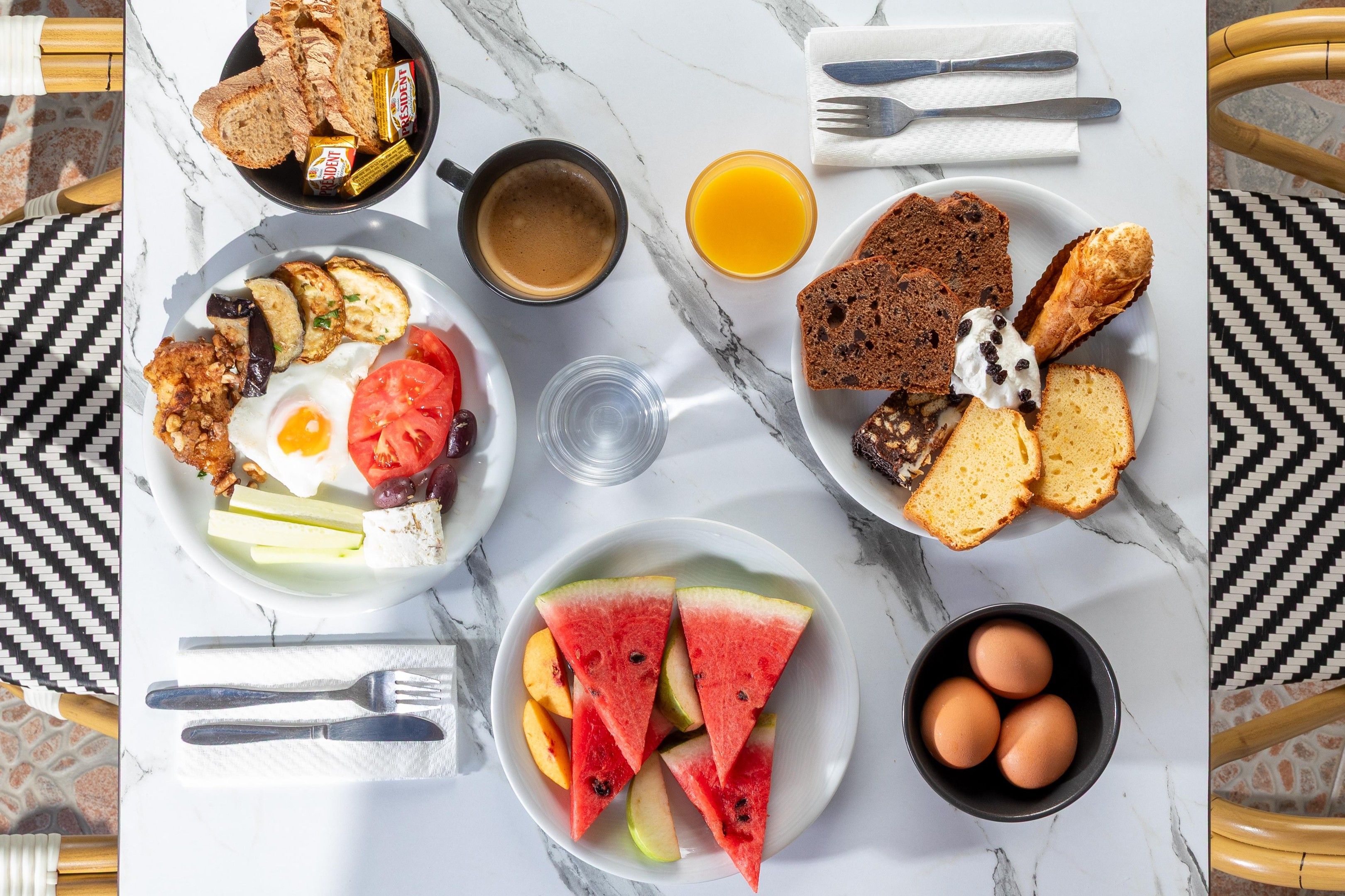A breakfast table with plates of food, a cup of coffee, a glass of orange juice, and a bowl of eggs.
