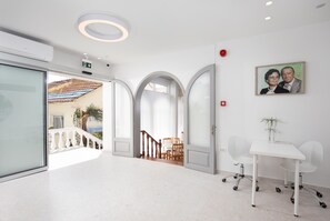 Un hall d’hôtel moderne avec un comptoir d’accueil blanc, un escalier et un espace repas visible à travers une porte ouverte.