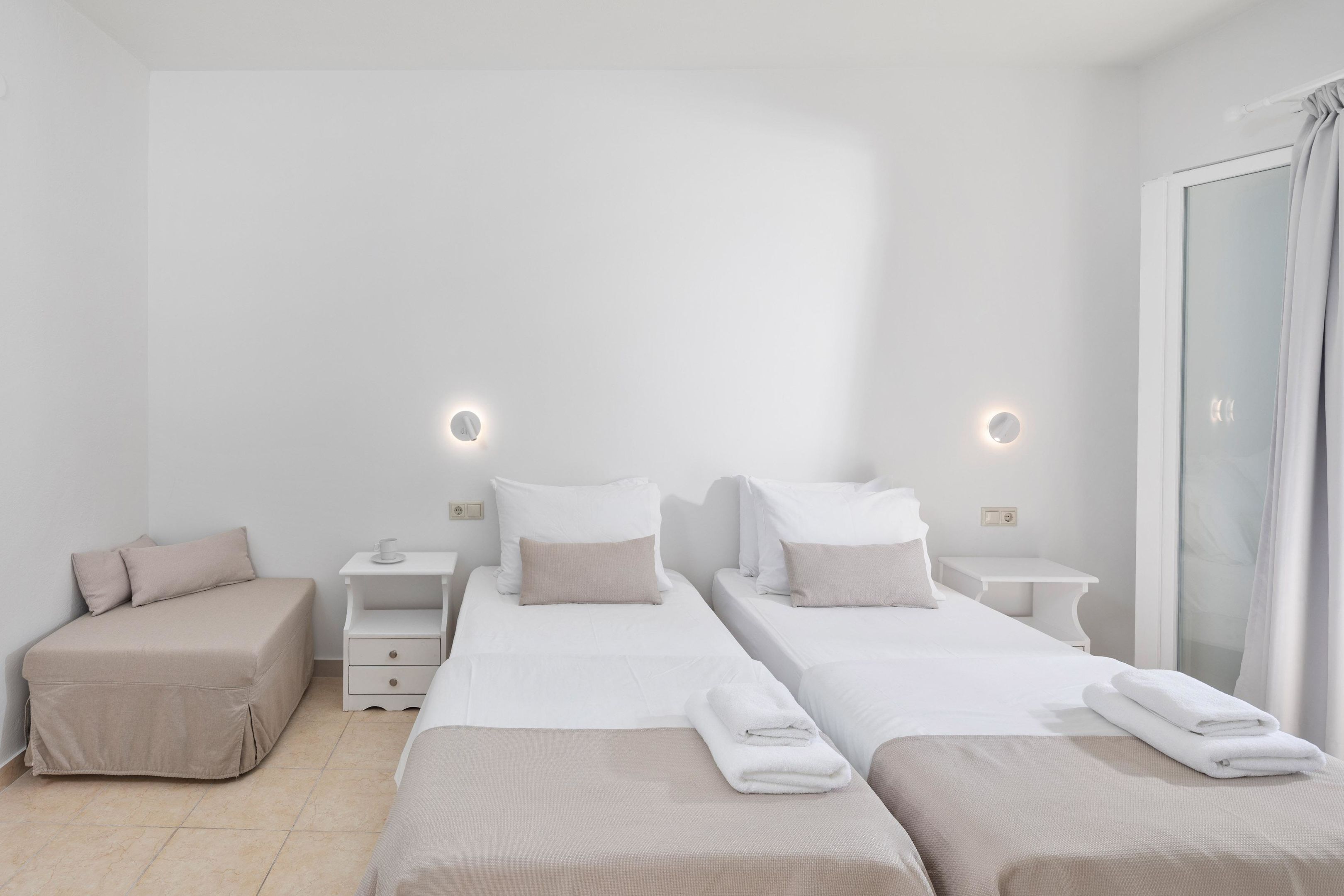 A hotel room with two single beds, a sofa, a small table, and a mirror.