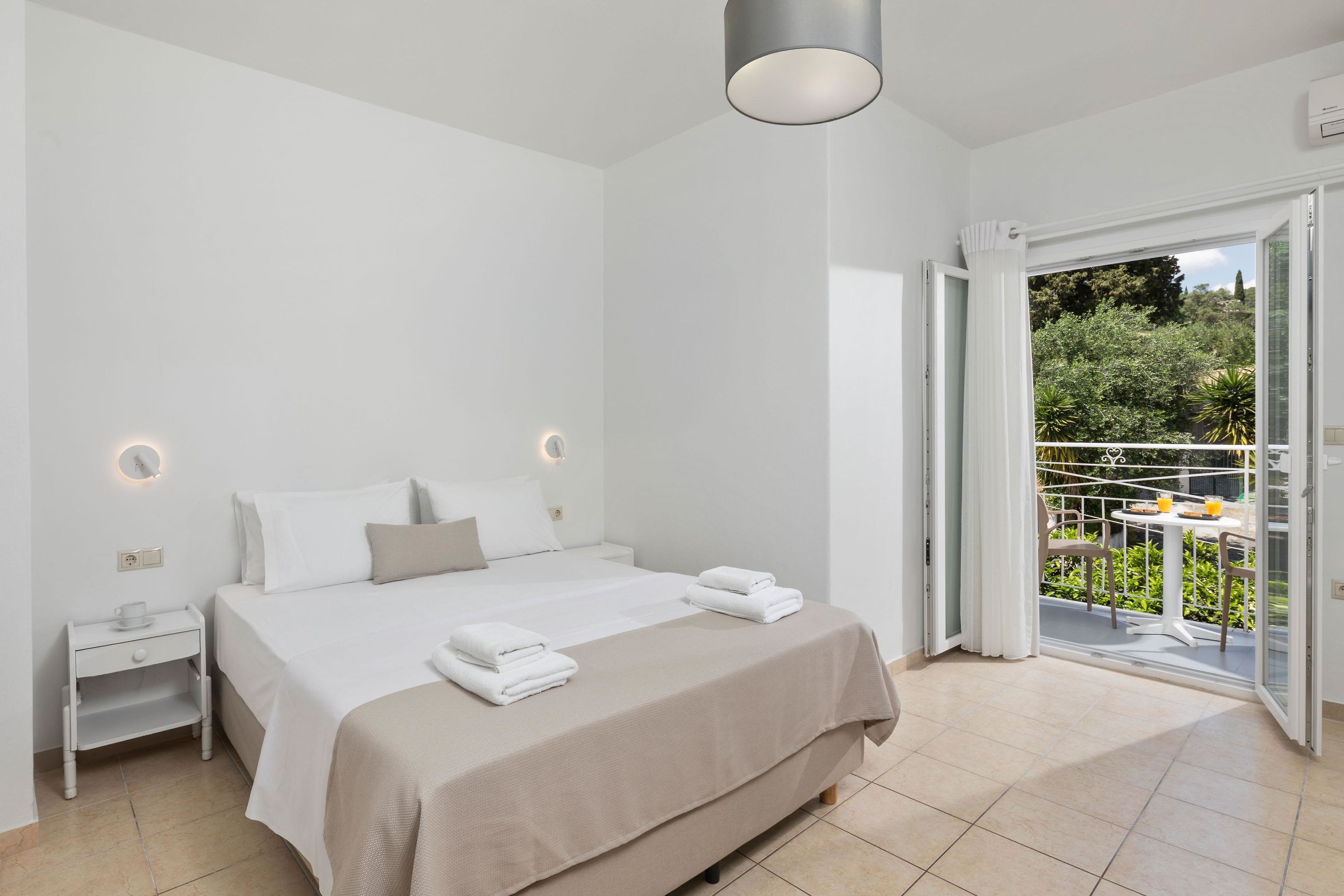 A bedroom with a bed, bedside table, and a view of a balcony with outdoor furniture.