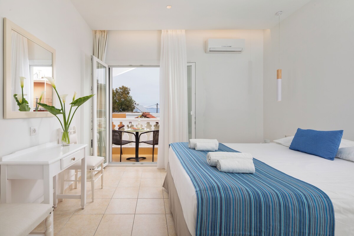 Habitación de hotel con cama, escritorio, silla, espejo y vista al exterior.