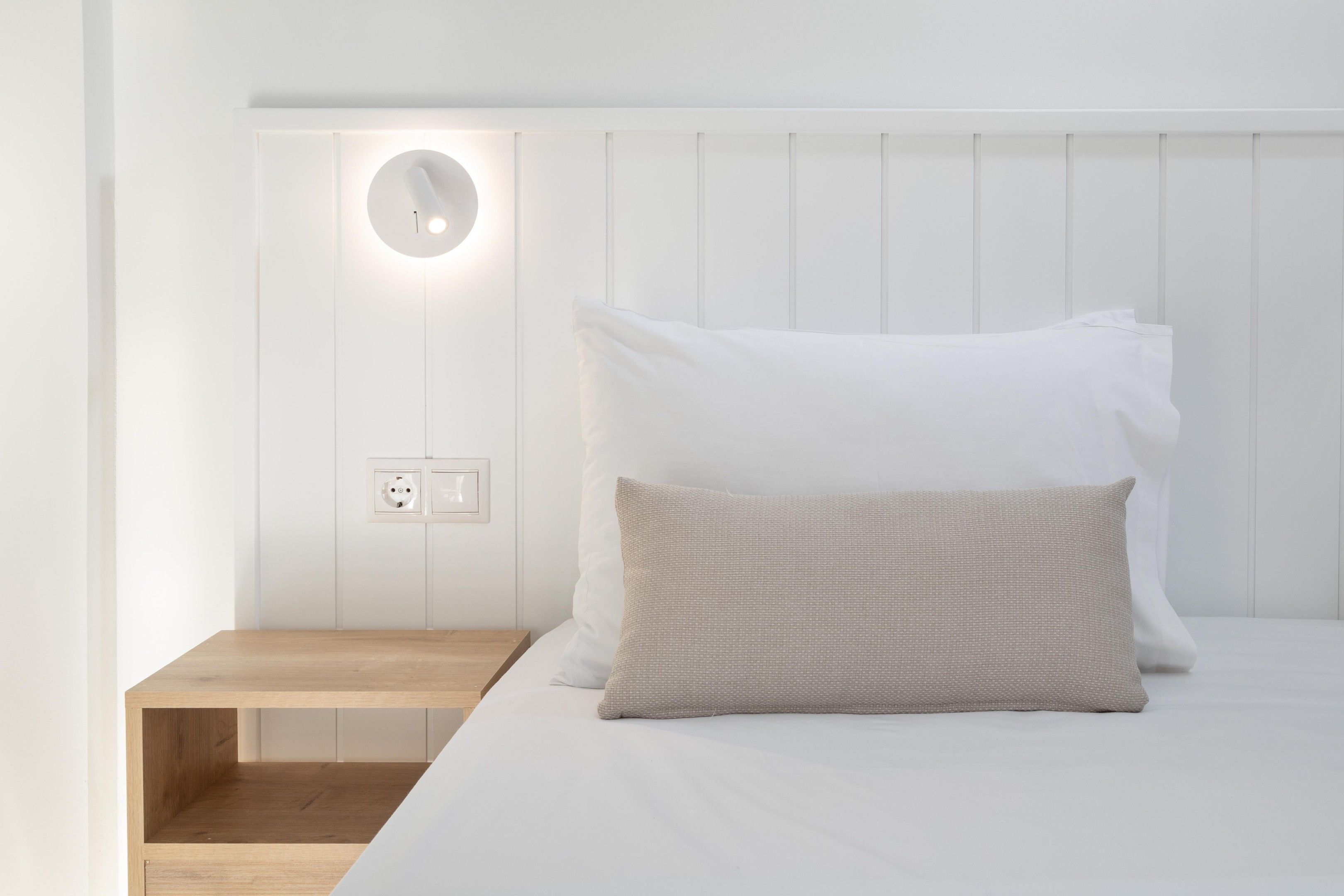 A minimalist bedroom with a single bed, a bedside table, and a wall-mounted light fixture.