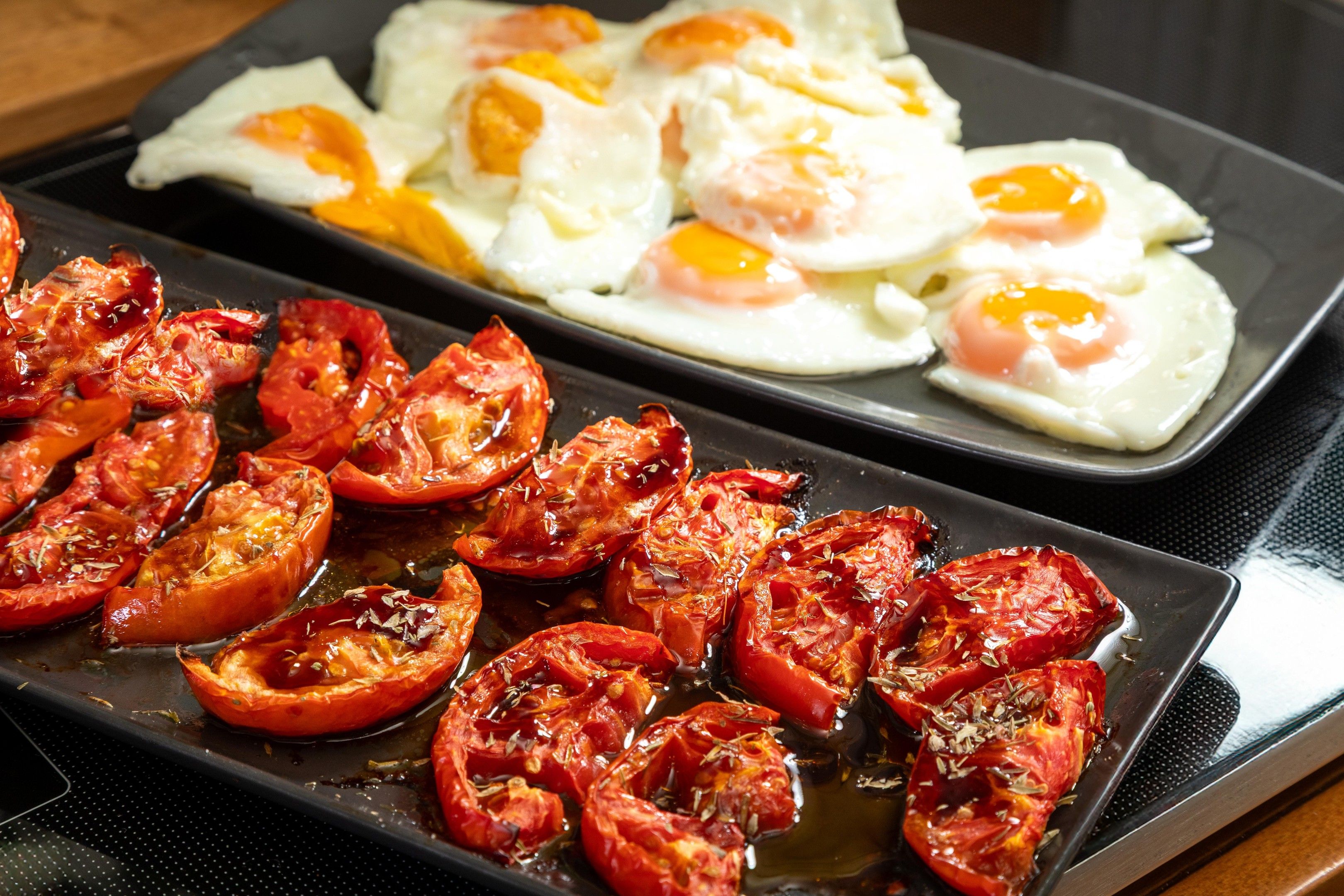 Eine Küchenarbeitsplatte mit einer Pfanne voller Tomatenscheiben und einer Pfanne mit gebratenen Eiern.