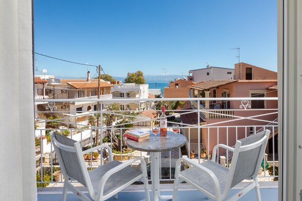 Un balcón con una mesa y dos sillas, con vistas a un pueblo costero y al mar.