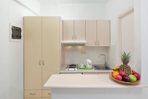 A compact kitchen with beige cabinets, a white countertop, a built-in stove, and a fruit bowl. - Bella Vista Beach Hotel and Studios (Corfu)
