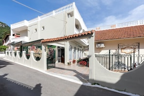 A two-story building with a white exterior, a tiled roof, and a gated entrance. - Bella Vista Beach Hotel and Studios (Corfu)