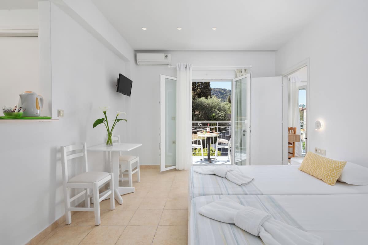 Une chambre d’hôtel moderne équipée d’un lit, d’une petite table avec des chaises, d’un téléviseur fixé au mur et d’un balcon offrant une vue sur l’extérieur.