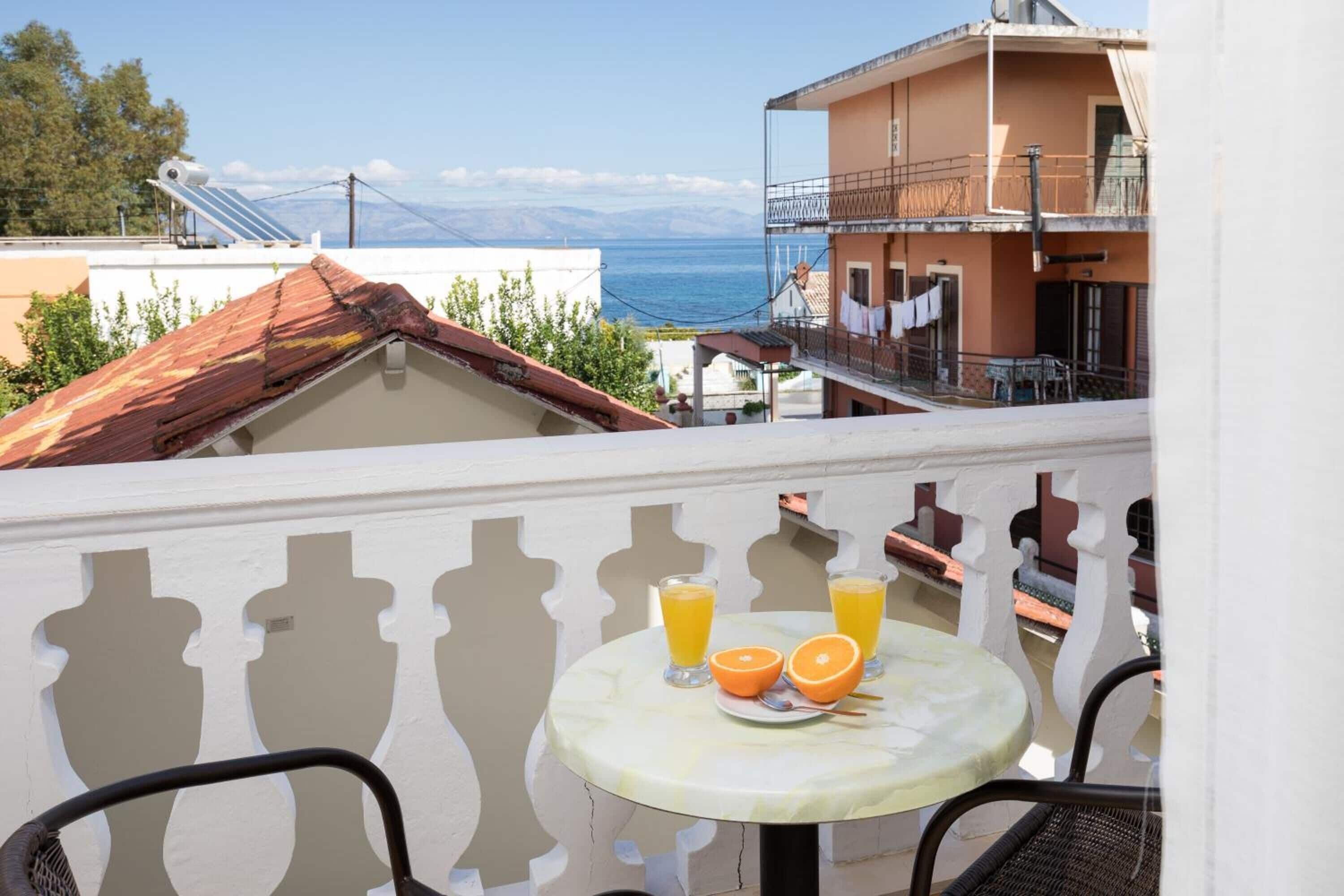 Un balcon avec une table dressée pour deux personnes, deux verres de jus d’orange et une assiette contenant deux moitiés d’une orange.