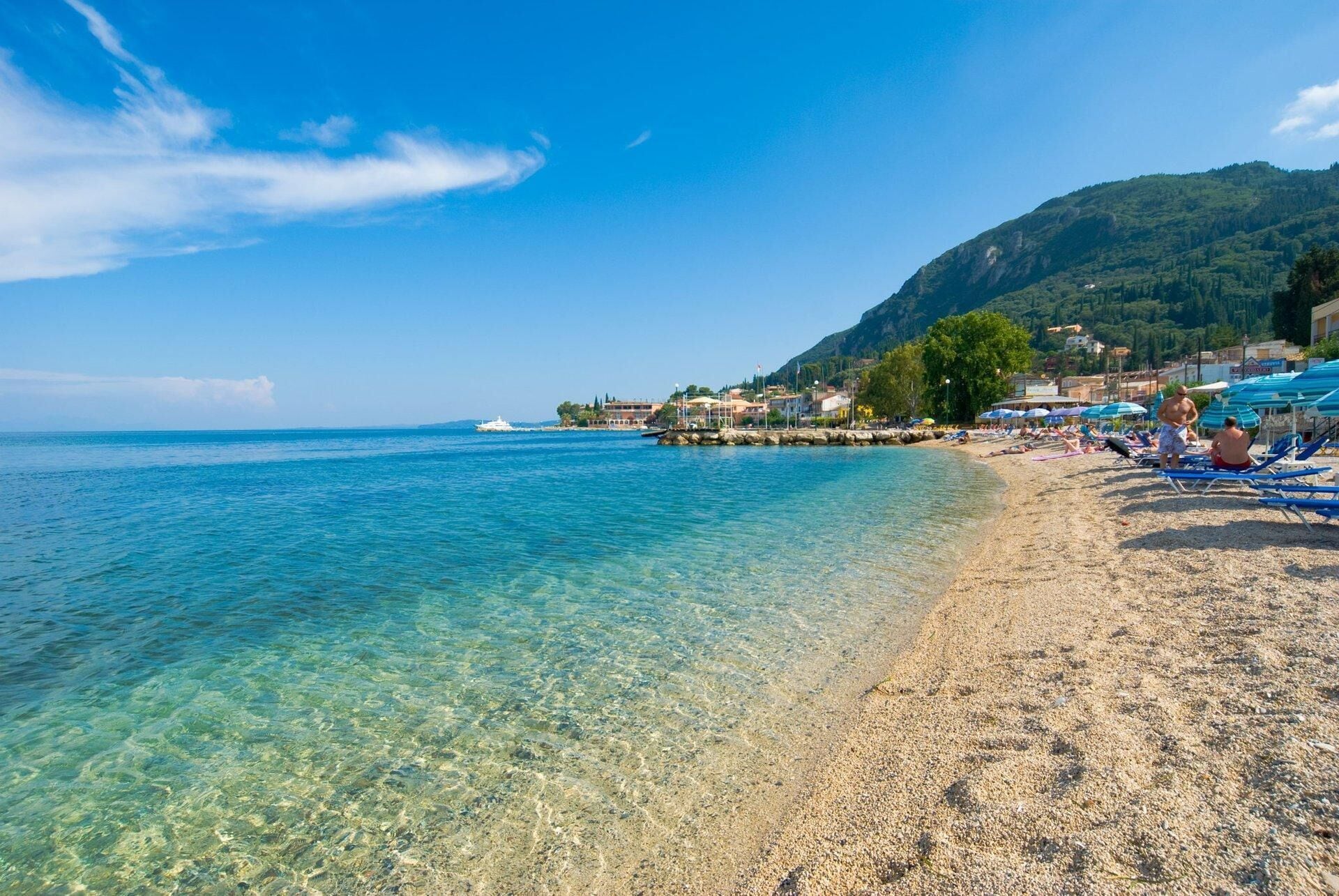 Una playa con aguas cristalinas y poco profundas, una costa rocosa y colinas al fondo.