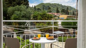 A balcony with a table set for breakfast, overlooking a lush landscape and a mountain.