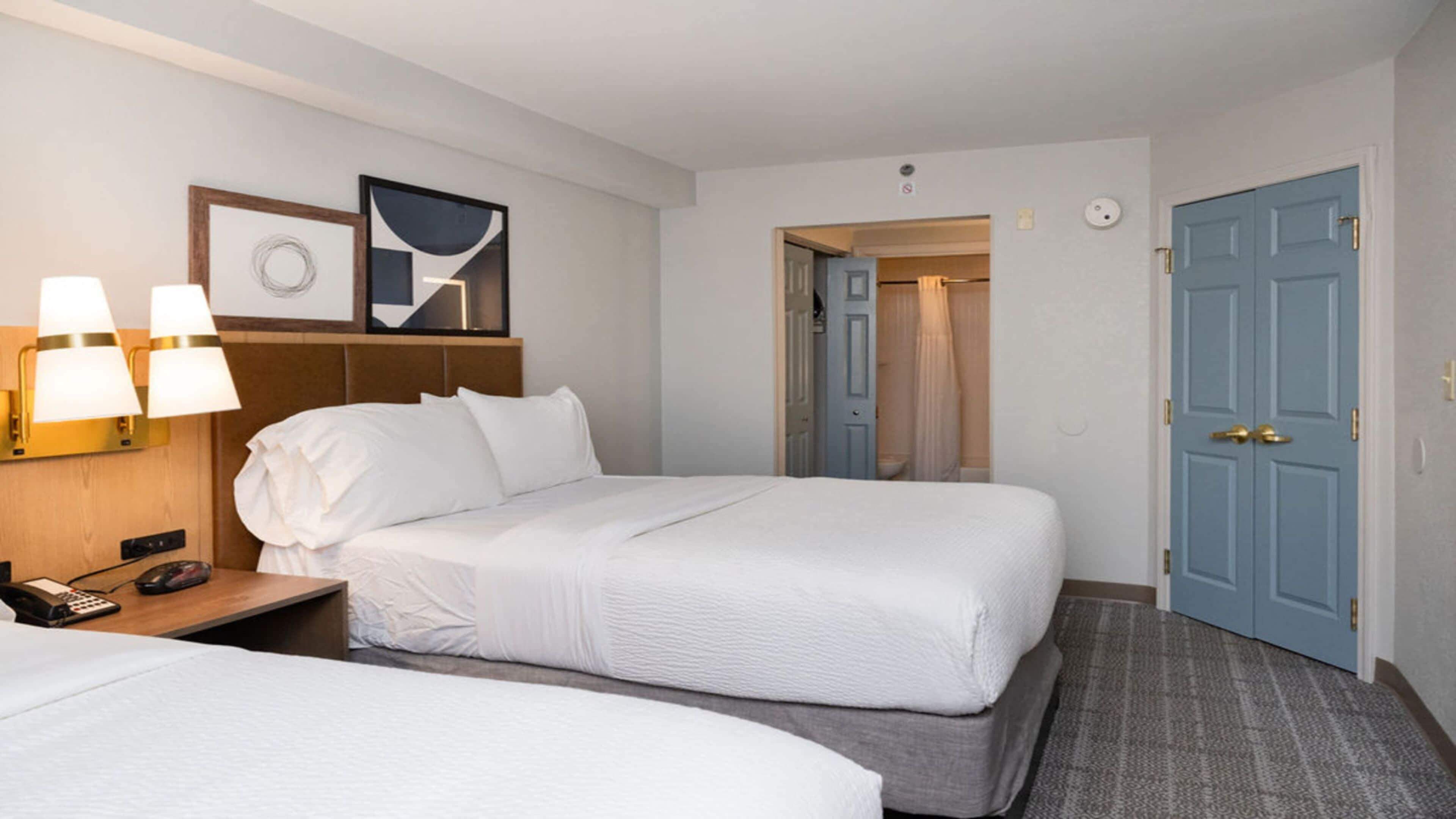 Een hotelkamer met twee bedden, een nachtkastje met een telefoon en lamp, een wandlamp en een deur naar de badkamer.