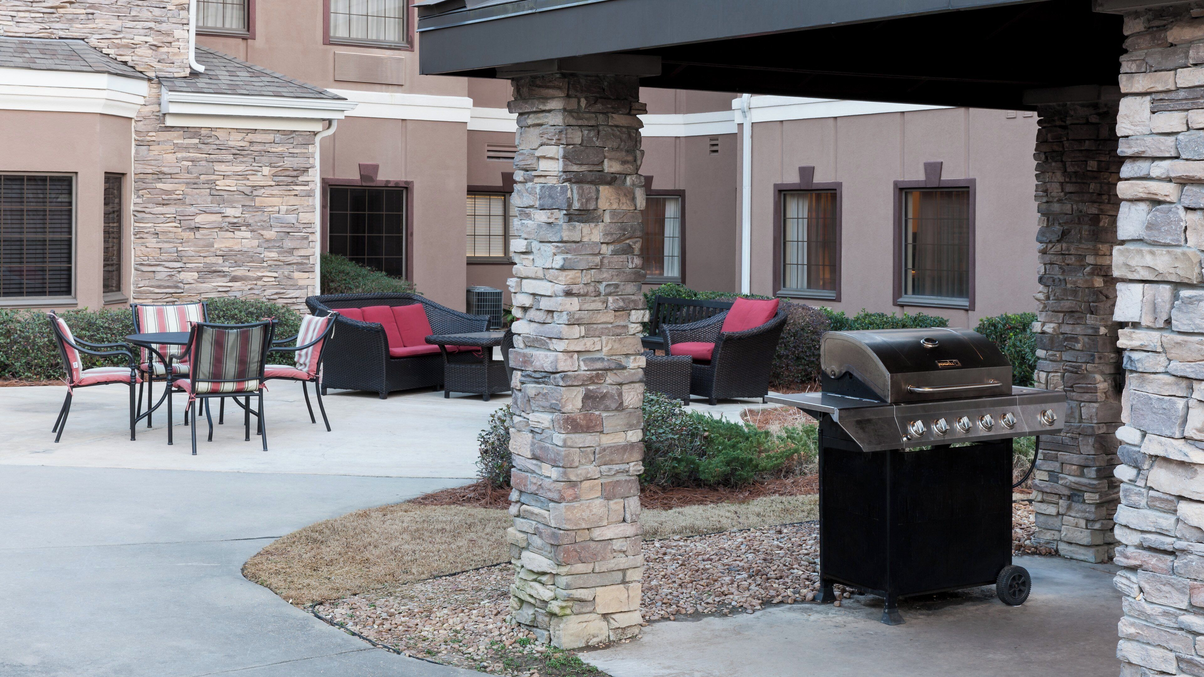 An outdoor patio area with stone pillars, a grill, and outdoor furniture.