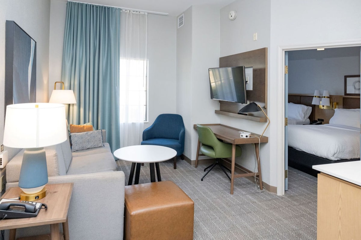 A hotel room with a bed, a desk, a chair, a TV, and a sofa.