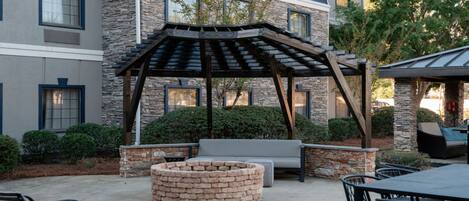 An outdoor patio area with a stone fire pit, seating, and a pergola structure.