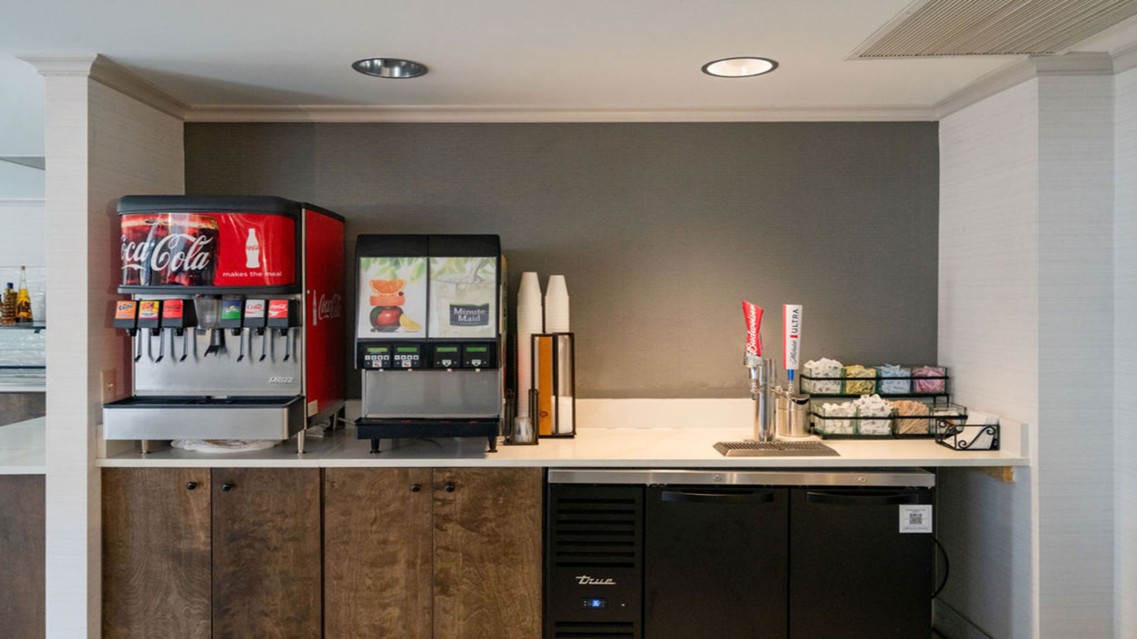 A self-service beverage station with Coca-Cola and Minute Maid options, a coffee machine, and a paper towel dispenser.